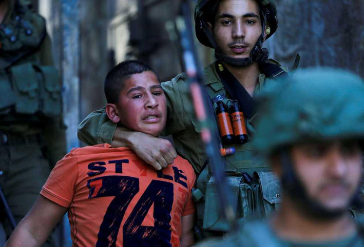 جندي إسرائيلي يمسك بطفل فلسطيني وسط مدينة الخليل